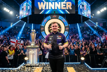 Luke Littler playing darts on stage during a professional tournament with fans watching